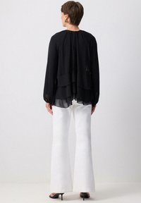 Sort lagd chiffon bluse med lange ærmer og rund hals, parret med hvide vidde ben bukser og sorte højhælede sko.