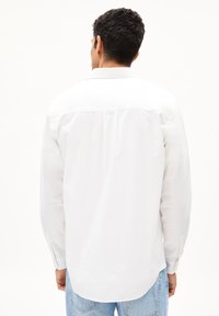 Camicia bianca a maniche lunghe realizzata in cotone, con polsini abbottonati e orlo curvo, caratterizzata da un design semplice e colletto classico.