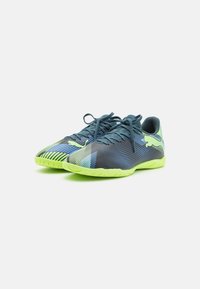Zapatillas deportivas con un upper azul oscuro, acentos verdes, acabado texturizado y una suela de goma con un patrón de relieve único. Incluye cordones.