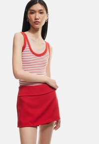 Top tipo tank rojo con canalé y rayas blancas y rojas, combinado con una falda mini roja ajustada que presenta una textura suave y una cinturilla doblada.