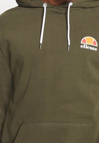 Felpa verde oliva con tasca a marsupio, coulisse bianche e logo circolare arancione e giallo con il testo "ellesse". Tessuto morbido.