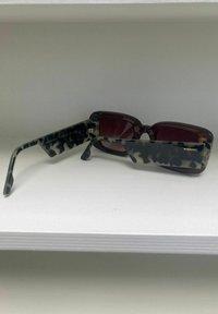 Zonnebril met een schildpadprint montuur dat een mix van donkere en lichte kleuren heeft, bruine glazen en merkvermelding op de arm.