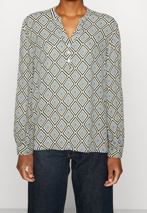 Person trägt ein langärmeliges Hemd mit blau-schwarzem Rautenmuster, kombiniert mit dunkelblauer Jeans.