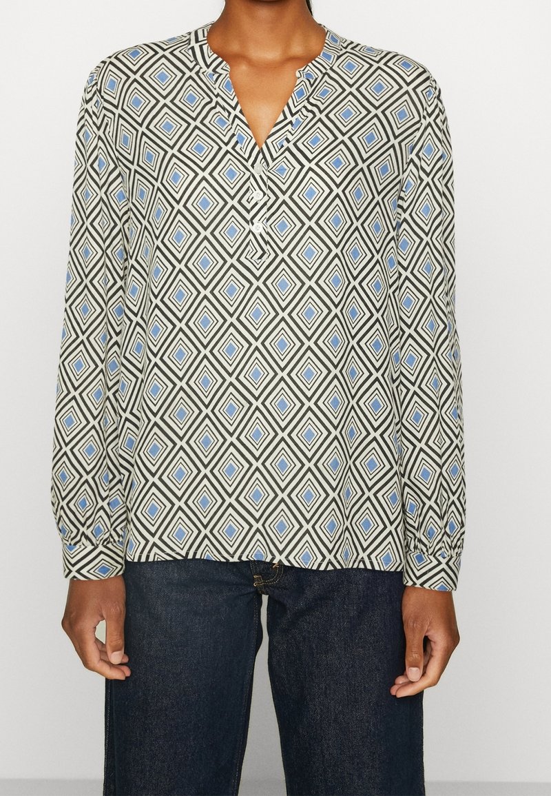 Personne portant une chemise à manches longues avec un motif en losanges bleu et noir, associée à un jean bleu foncé.