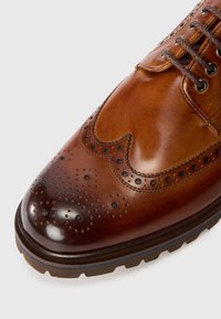 Chaussure brogue en cuir marron avec un bout poli, des perforations décoratives et une semelle en caoutchouc bleu contrastant. Design classique à lacets.