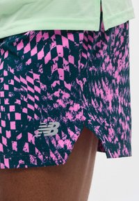 Roosa ja tumelilla mustriga spordipükste lähiplaan, millel on New Balance'i logo ja mida kantakse helerohelise pealsega.