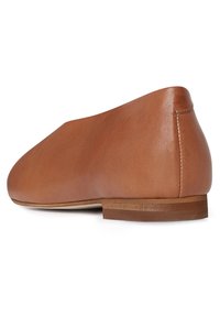 Zapato de cuero marrón claro con forma redondeada, tacón bajo y textura suave. Presenta una costura en la parte trasera y una suela de madera natural.