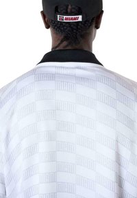 Witte geblokte jersey met daarop het woord "MIAMI" in een subtiel ruitpatroon, met een zwarte kraag en een achterstevoren gedragen pet.