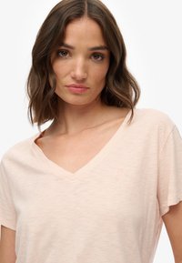Lyserød V-hals t-shirt lavet af blødt, tekstureret stof, med korte ærmer og et lille logo på brystet.