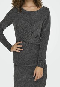 Robe ajustée à manches longues en noir avec des fils métalliques. Présente un détail avant torsadé et un tissu lisse et extensible pour plus de confort.