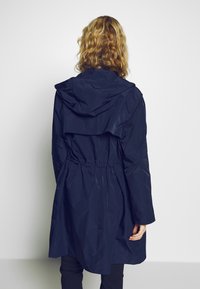 Námořnický voděodolný parka s kapucí, staženým pasem a vrstveným zadním designem. Hladká textura a dlouhé rukávy.