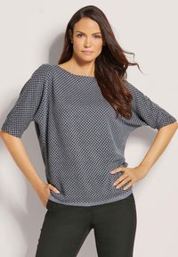 Grijze gebreide trui met een losvallende pasvorm, ronde halslijn en korte mouwen, met een stippenpatroon. Gecombineerd met zwarte broek.