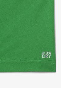 Grön textil med en texturerad yta, med en vit "ULTRA DRY"-logotyp vid fållen. Enkelt design utan ytterligare mönster eller accenter.