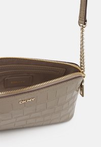 Borsa DKNY in materiale taupe texturizzato, con zip e hardware dorati, dotata di tracolla a catena e dettaglio del logo sulla parte frontale.