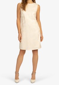 Bezramenné smetanově bílá šaty s texturovanou tkaninou, ke kolenům, s kulatým výstřihem a rovnou siluetou. V kombinaci s krémovými lodičkami.
