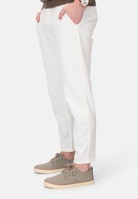 Weiße Hosen mit schlankem Design und Seitentaschen, kombiniert mit hellgrauen Schuhen, die eine strukturierte Oberseite und eine tanfarbene Sohle haben.