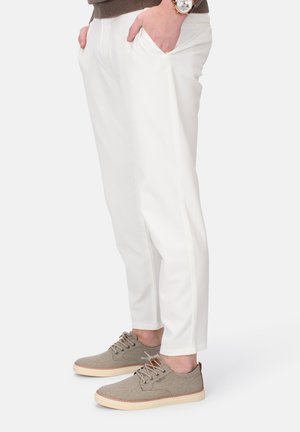 Weiße Hosen mit schlankem Design und Seitentaschen, kombiniert mit hellgrauen Schuhen, die eine strukturierte Oberseite und eine tanfarbene Sohle haben.