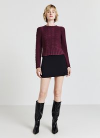Maglione a maglia bordeaux con motivi testurizzati e orlo svasato, abbinato a una minigonna nera aderente e stivali neri sopra il ginocchio.
