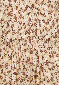 Robe fleurie en beige avec des fleurs roses et brunes éparpillées. Elle possède une taille froncée, une jupe fluide et un tissu léger.