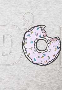 Grått tyg med en stor, färgstark donutgrafik, med en bitad kant, rosa glasyr och flerfärgade strössel. Subtil präglad text i närheten.