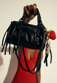 Black leather handbag with textured surface, braided handles, and colorful charm featuring a red strawberry and assorted beads.