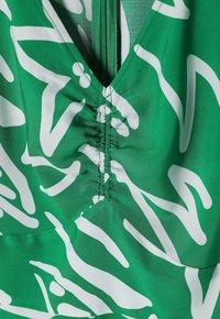 Tissu vert avec motif abstrait blanc, avec une couture froncée et une fermeture éclair verticale verte au centre.