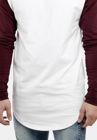 Fehér, hosszú ujjú ing bordó ujjakkal, pamut anyagból, ívelt aljjal, slim fit szabással, látható kézi részletekkel és világoskék farmernadrággal.