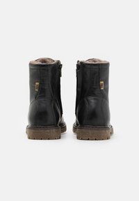 Botines de cuero negros a la altura del tobillo con cremallera lateral, forrados con material suave y con una suela de goma texturizada para un mejor agarre.