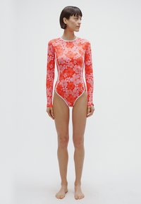 Červené plavky s dlouhými rukávy se květinovým vzorem v odstínech růžové. Vyrobené z elastického materiálu, s kontrastními bílými detaily a vysokým límcem.