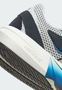 Sportska cipela s laganim mrežastim gornjim dijelom u bijeloj i mornarsko plavoj boji, s teksturiranim potplatom i logotipom "LIGHTSTRIKE" na srednjem potplatu.