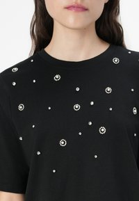 T-shirt noir avec des embellissements dispersés de strass ronds et de perles, créant une apparence décorative et texturée.