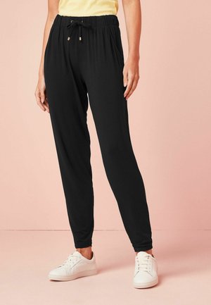 Svarta joggingsbyxor med elastiskt midjeband och justerbar snörning, tillverkade av ett mjukt och lätt tyg. Bärs tillsammans med vita sneakers.