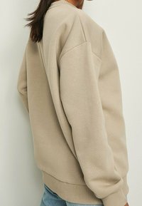 Felpa beige con una vestibilità rilassata, scollatura rotonda e polsini a coste. Realizzata in morbido tessuto misto cotone, presenta dettagli di design minimalisti.