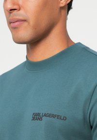 Mėlynos spalvos medvilnės džemperis su apvaliomis iškirptėmis, su juodu "KARL LAGERFELD JEANS" logotipu ant krūtinės ir lygia tekstūra.
