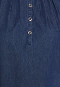 Džínová šaty v tmavě modré barvě s jemnou texturou, s knoflíkovou légu na přední straně a šesti lesklými kulatými knoflíky.