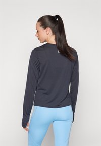 Camisa de manga larga, de color azul marino oscuro, hecha de tejido elástico, con cuello redondo y un detalle del logo en la parte trasera, combinada con leggings de color azul claro.