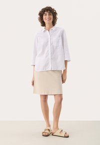 Hvid linned skjorte med lange ærmer, parret med en beige knælang nederdel og lyse sandaler. Simple design og teksturer.