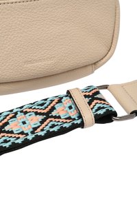 Beige läderväska med texturerad yta, med ett färgglatt vävt bälte i svarta, blå och aprikosmönster, fäst med silverfärgad hårdvara.
