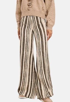 Pantalones anchos y holgados con rayas verticales negras y beige, llevados con un jersey beige y zapatos topo sobre un fondo blanco.