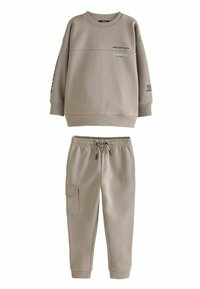 Beige fleece collegepaita ja siihen sopivat verkkarit, joissa on pyöreä kaula-aukko, pudotetut olkapäät, sivutaskut ja painettu teksti hihoissa.