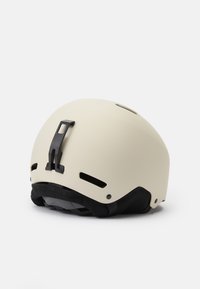 Bijela mat kaciga s crnim akcentima i ventilacijskim otvorima. Ima podesivu trakicu i stražnji kopču za prilagodbu. Glatka tekstura.