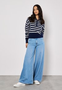 Marineblau-weiß gestreifter Strickpullover mit Kragen und geripptem Saum, kombiniert mit hellblauen Weitenjeans und weißen Sneakers.