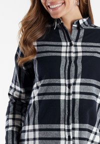 Camisa a cuadros en negro y gris, hecha de una tela suave, con cierre de botones en la parte delantera, cuello y mangas largas con un ajuste relajado.