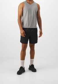 Graues ärmelloses Sport-Tanktop, schwarze Shorts, weiße Socken und schwarze Sneakers. Einfaches Design mit minimalen Logos und Akzenten.