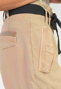 Beige cargoshorts met een zwarte elastische tailleband, een zijzak met gestikte accenten en een zachte katoenstof.