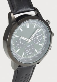 Zegarek chronograf z czarną stalową kopertą, ciemnozieloną tarczą, srebrnymi znacznikami godzin oraz czarnym, perforowanym paskiem skórzanym.