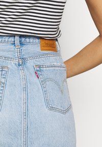 Jeans in denim azzurro chiaro presentano una vita alta, due tasche posteriori e un'etichetta in pelle marrone sulla vita con dettagli in rilievo.