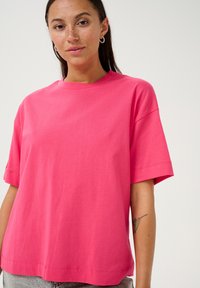 Lyserød bomulds T-shirt med rund halsudskæring, korte ærmer og afslappet pasform. Har synlige sømme langs kanten og ærmeenderne.