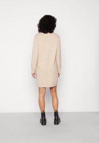 Vestido de punto beige con mangas largas, un corte relajado y puños acanalados, combinado con botas negras hasta el tobillo de suela gruesa.
