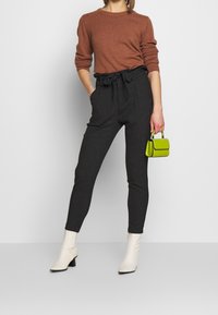 Brown knit sweater, high-waisted black pants with belt, white ankle boots, and a small green handbag. Simple design and textured materials.